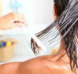 Kobieta po kąpieli, stoi tyłem do obiektywu, nakłada na włosy odżywkę i rozczesuje je grzebieniem.